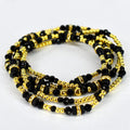 Four strands of black and gold beaded jewelry. The strands are intertwined, showcasing a mix of small gold beads, larger black beads, and gold-toned spacers with clear crystal accents. The jewelry is displayed on a white background.