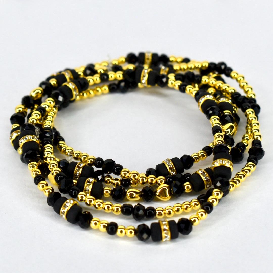 Four strands of black and gold beaded jewelry. The strands are intertwined, showcasing a mix of small gold beads, larger black beads, and gold-toned spacers with clear crystal accents. The jewelry is displayed on a white background.