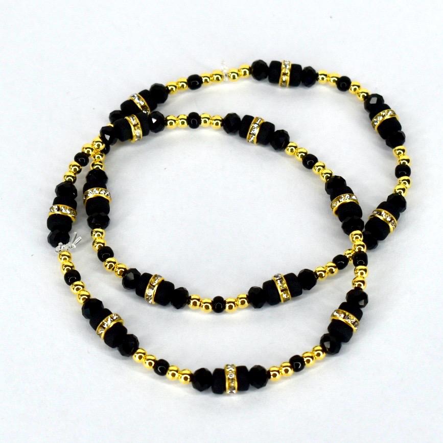 A set of two black beaded bracelets with gold-colored accents and rhinestone-studded spacers. The bracelets feature small, round gold beads and larger, faceted black beads. The design is symmetrical, with the beads arranged in a repeating pattern.