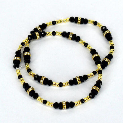 A set of two black beaded bracelets with gold-colored accents and rhinestone-studded spacers. The bracelets feature small, round gold beads and larger, faceted black beads. The design is symmetrical, with the beads arranged in a repeating pattern.