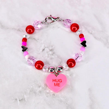 Tumbler handle bracelet with red pink and crystal beads and a conversation heart charm that says 'hug me' in the center. There is a silver lobster clasp at the top of the mini bracelet to keep the ends together.