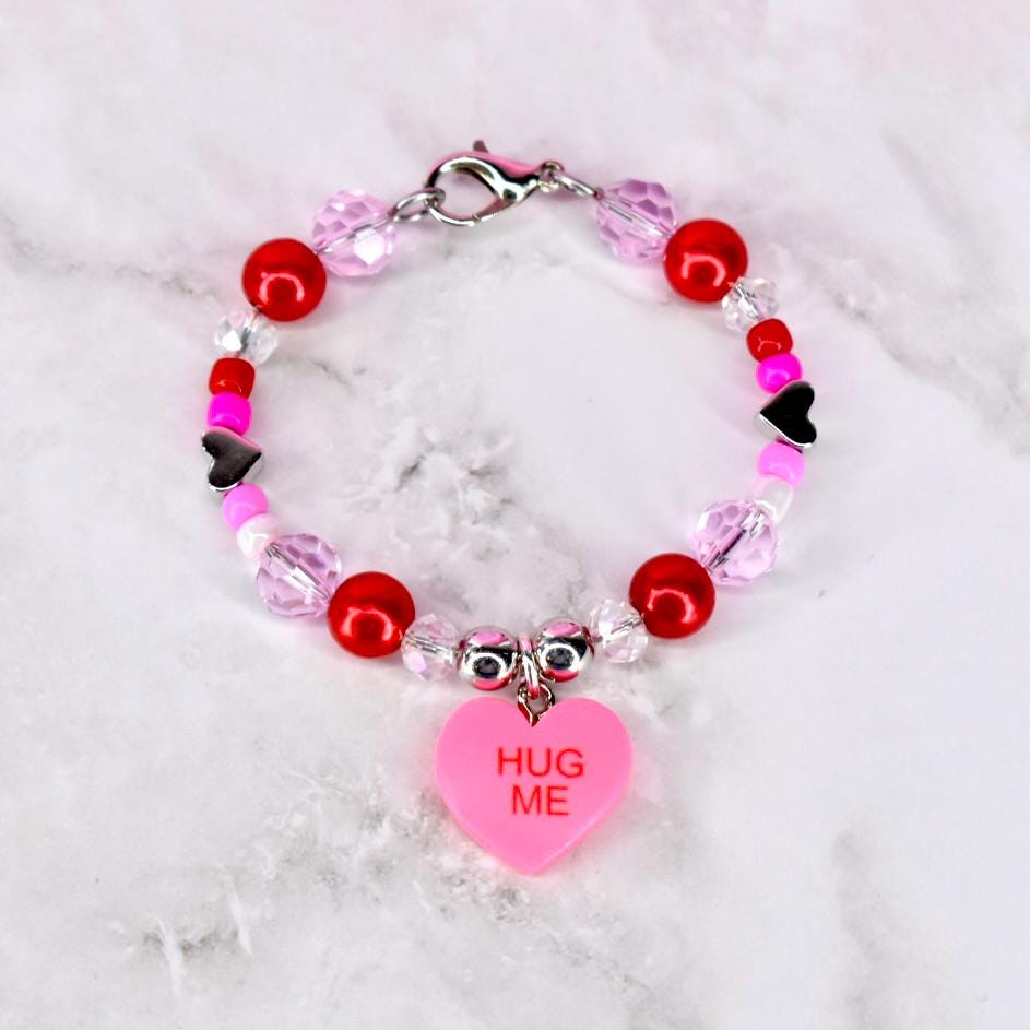 Tumbler handle bracelet with red pink and crystal beads and a conversation heart charm that says 'hug me' in the center. There is a silver lobster clasp at the top of the mini bracelet to keep the ends together.
