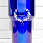 A blue tumbler with a beaded bracelet. The bracelet features clear, blue, and pink beads, with a star charm. The tumbler has a gradient finish, transitioning from blue to purple.