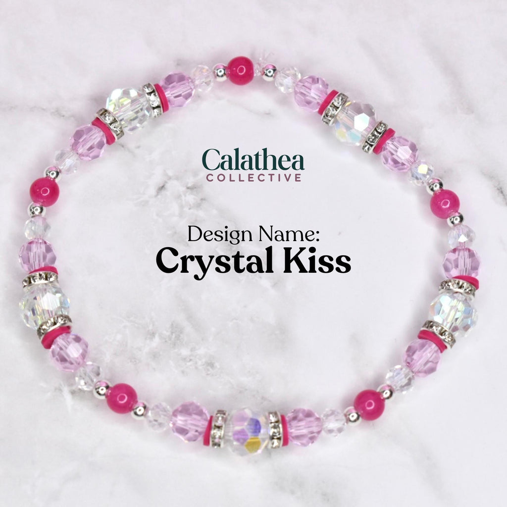 A beaded bracelet with the text "Calathea Collective" and "Design Name: Crystal Kiss". The bracelet features pink, clear, and silver beads. The bracelet is on a white and gray marble surface.
