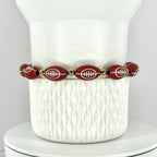 A football-themed bracelet. The bracelet features oval-shaped beads with white football designs, interspersed with gold-colored beads. The bracelet is displayed on a white, textured surface.
