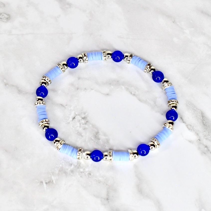 A light blue and silver beaded bracelet. The bracelet features alternating light blue disc-shaped beads and silver-colored cylindrical beads. Dark blue round beads are interspersed throughout the design.