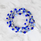 A collection of blue beaded bracelets with silver accents and clear crystal beads. The bracelets feature various shades of blue, including light and dark hues, and are arranged in a layered design. The beads are strung together with a silver-colored material.