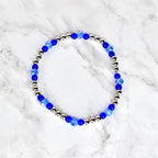 A beaded bracelet featuring alternating silver-colored beads and vibrant blue beads. The bracelet's design incorporates a mix of round and faceted beads, creating a sparkling and eye-catching accessory. The bracelet is displayed on a white marble surface.