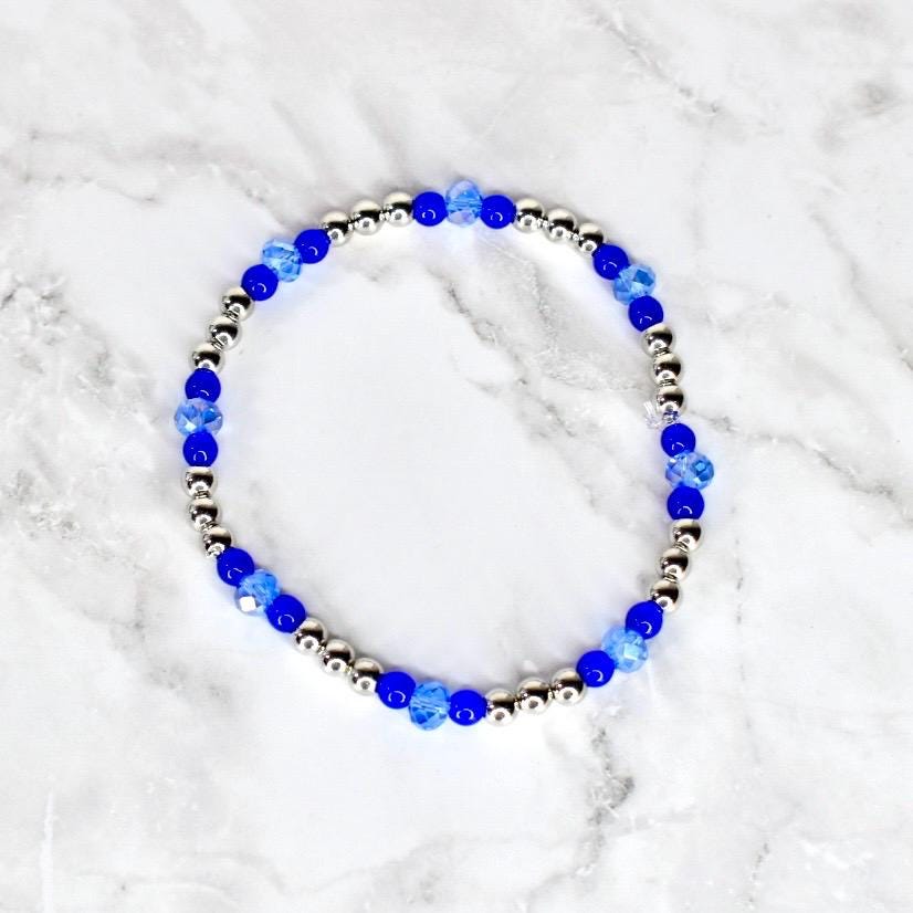 A beaded bracelet featuring alternating silver-colored beads and vibrant blue beads. The bracelet's design incorporates a mix of round and faceted beads, creating a sparkling and eye-catching accessory. The bracelet is displayed on a white marble surface.