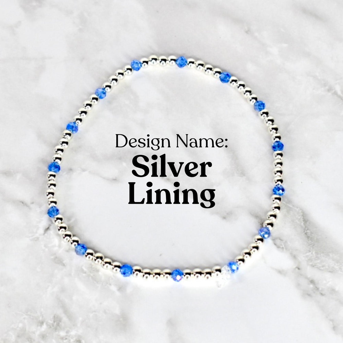 A silver beaded bracelet with blue crystal accents. The bracelet is circular and features the text "Design Name: Silver Lining" in black font. The bracelet is displayed on a white and gray marble surface.
