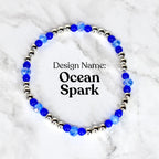 A beaded bracelet with the text "Design Name: Ocean Spark". The bracelet features alternating silver-colored beads and blue faceted beads. The bracelet is displayed on a white and gray marble surface.