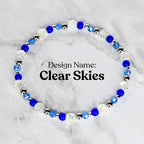 A beaded bracelet with the design name "Clear Skies." The bracelet features a circular arrangement of clear, blue, and silver beads. The beads are a mix of faceted and round shapes, creating a sparkling effect. The text "Design Name: Clear Skies" is displayed.