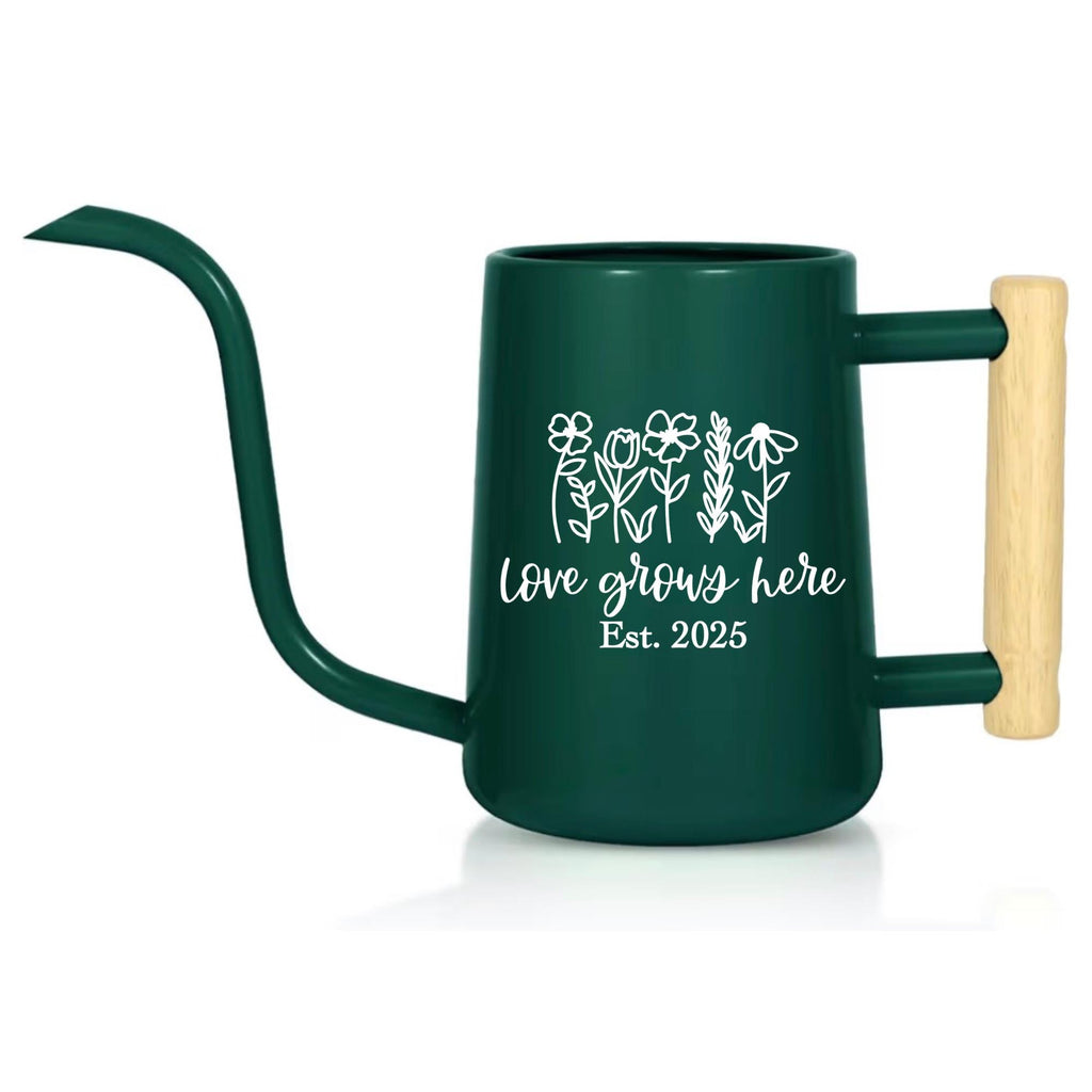 A dark green metal watering can with a long, curved spout and a wooden handle. The can features white floral line art and the text "love grows here Est. 2025". Ideal for gardening and plant care.