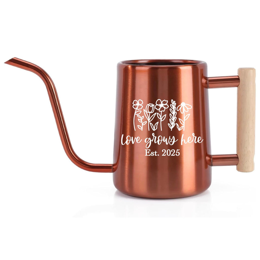Copper-colored watering can with a long spout and wooden handle. The can features a white floral design and the text "Love grows here Est. 2025". Ideal for indoor or outdoor gardening, this watering can is a stylish addition.