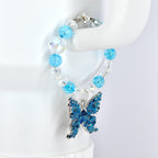 A beaded tumbler handle charm featuring a blue butterfly charm. The bracelet has light blue and clear beads. The butterfly charm is detailed with blue enamel and silver-tone metal. The bracelet is secured with a silver-tone clasp.