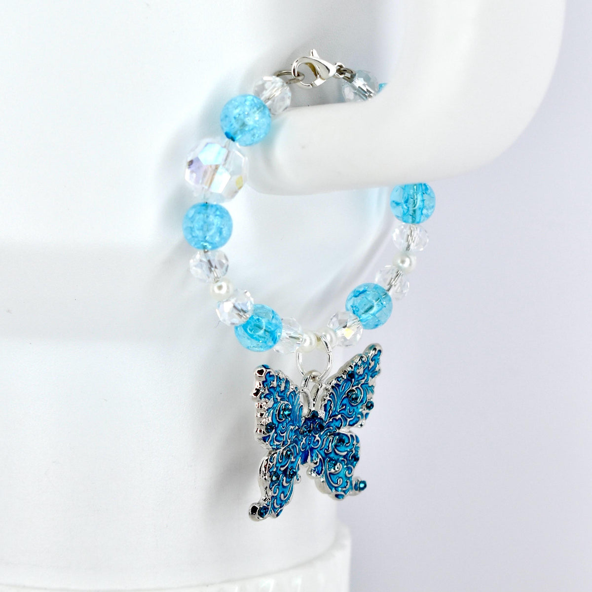A beaded tumbler handle charm featuring a blue butterfly charm. The bracelet has light blue and clear beads. The butterfly charm is detailed with blue enamel and silver-tone metal. The bracelet is secured with a silver-tone clasp.