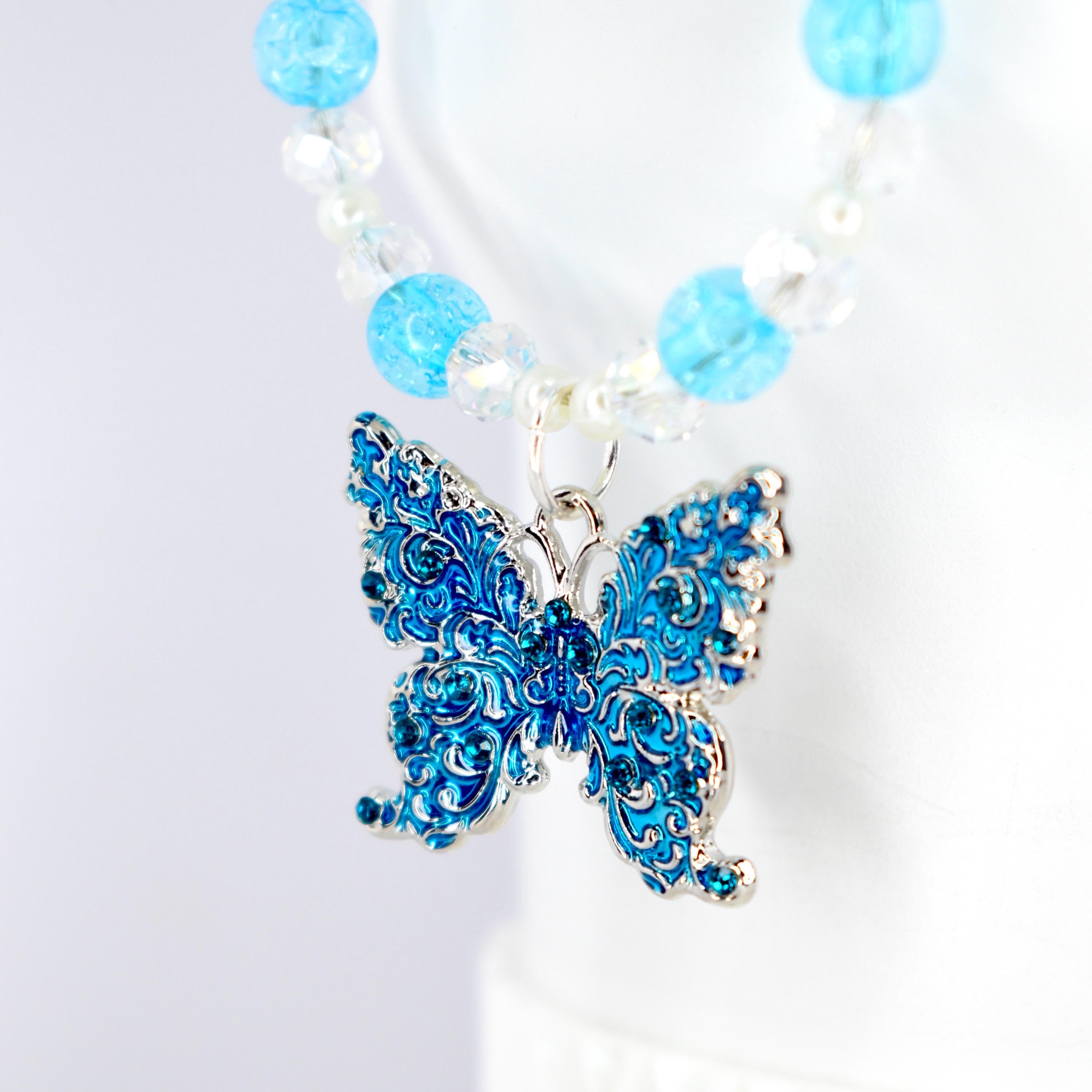 A blue butterfly pendant tumbler handle charm with intricate detailing and silver-colored trim. The butterfly is adorned with small blue crystals. The handle charm features a strand of clear and light blue beads.