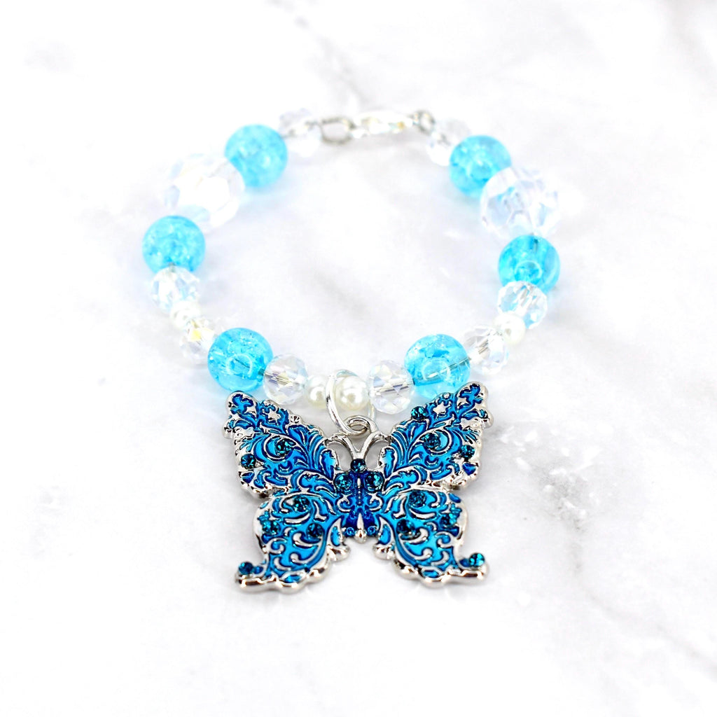 A beaded tumbler handle charm featuring a detailed blue butterfly pendant. The handle charm has clear and light blue beads, with a silver-tone clasp. The butterfly pendant is adorned with intricate patterns and small blue gemstones.
