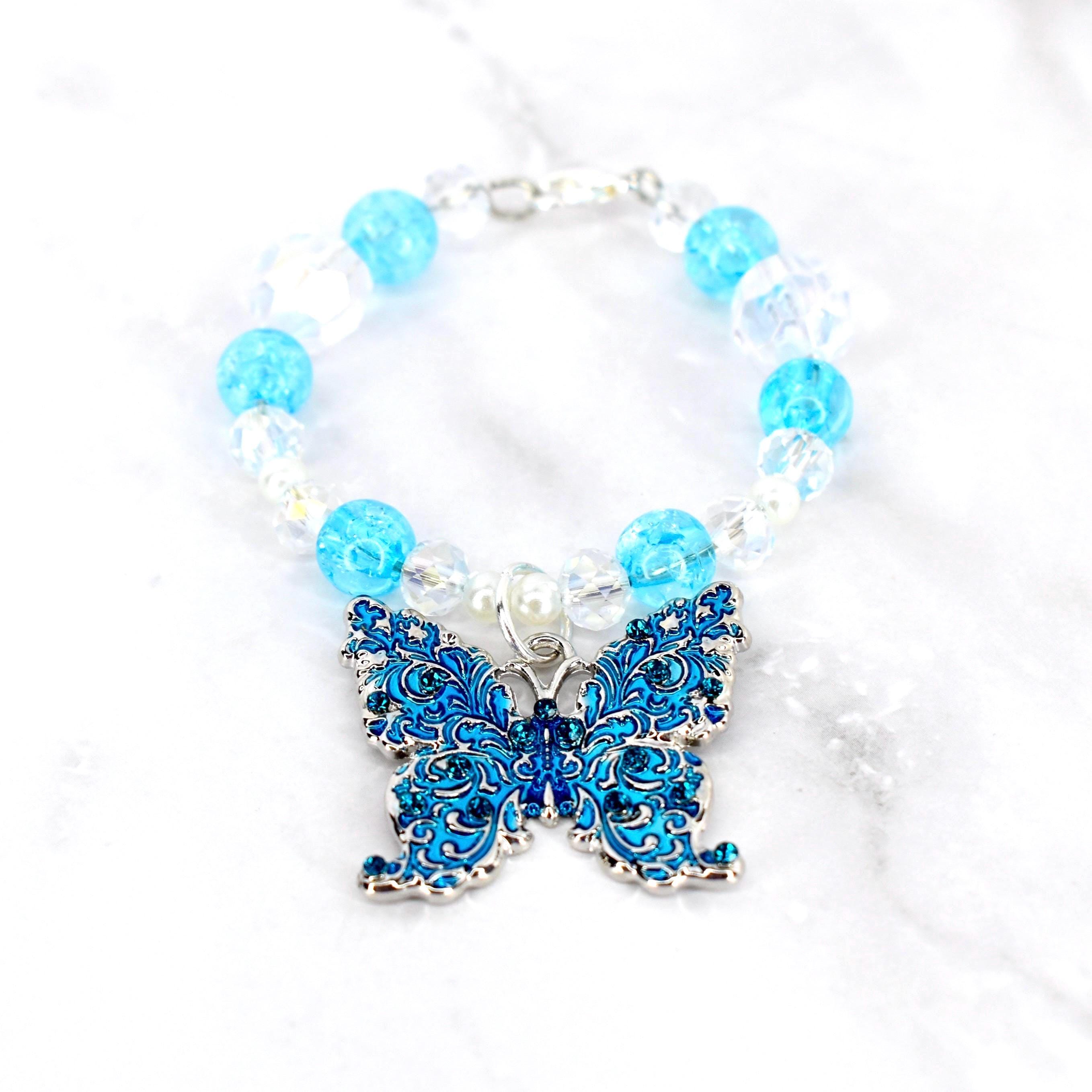 A beaded tumbler handle charm featuring a detailed blue butterfly pendant. The handle charm has clear and light blue beads, with a silver-tone clasp. The butterfly pendant is adorned with intricate patterns and small blue gemstones.