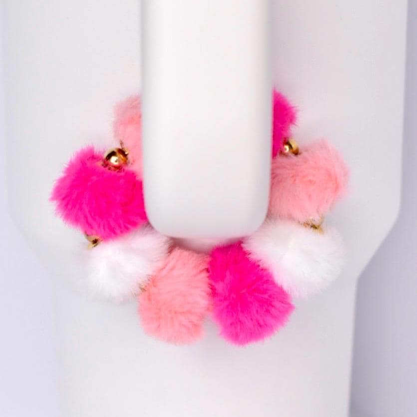 A vibrant bracelet featuring a series of fluffy pom-poms in shades of pink and white. The pom-poms are arranged in a circular pattern, with gold-colored accents. The bracelet is set against a white background.