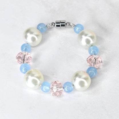 A tumbler handle bracelet featuring large, white faux pearls, light blue beads, and faceted pink crystal beads. The bracelet is connected with a silver-colored magnetic clasp. The beads are strung together to form a circular shape.