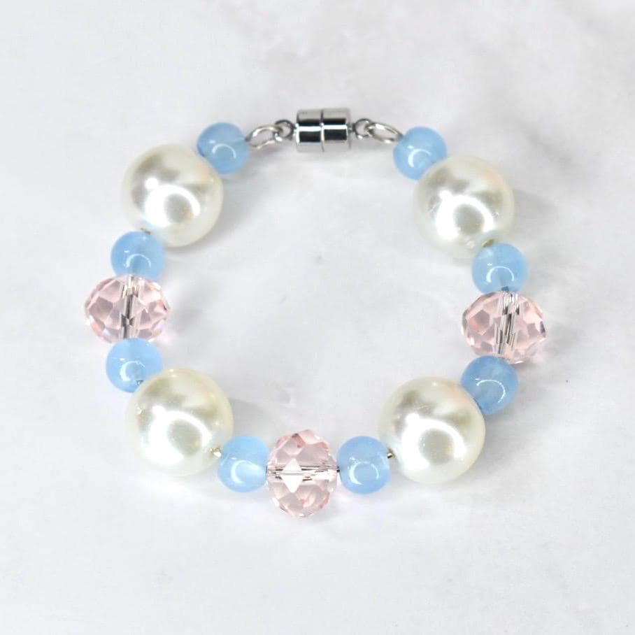 A tumbler handle bracelet featuring large, white faux pearls, light blue beads, and faceted pink crystal beads. The bracelet is connected with a silver-colored magnetic clasp. The beads are strung together to form a circular shape.