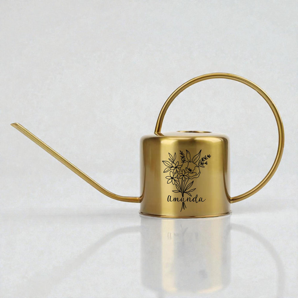 A gold metal watering can with a long spout and a curved handle. The can features a black floral design and the name "Amanda" in script. The watering can is designed for indoor or outdoor plant care.