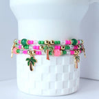 Set of vibrant tropical-themed tumbler bracelets featuring green and pink beads, gold accents and palm tree charms, styled on a white Stanley tumbler—perfect handmade summer boho jewelry stack.