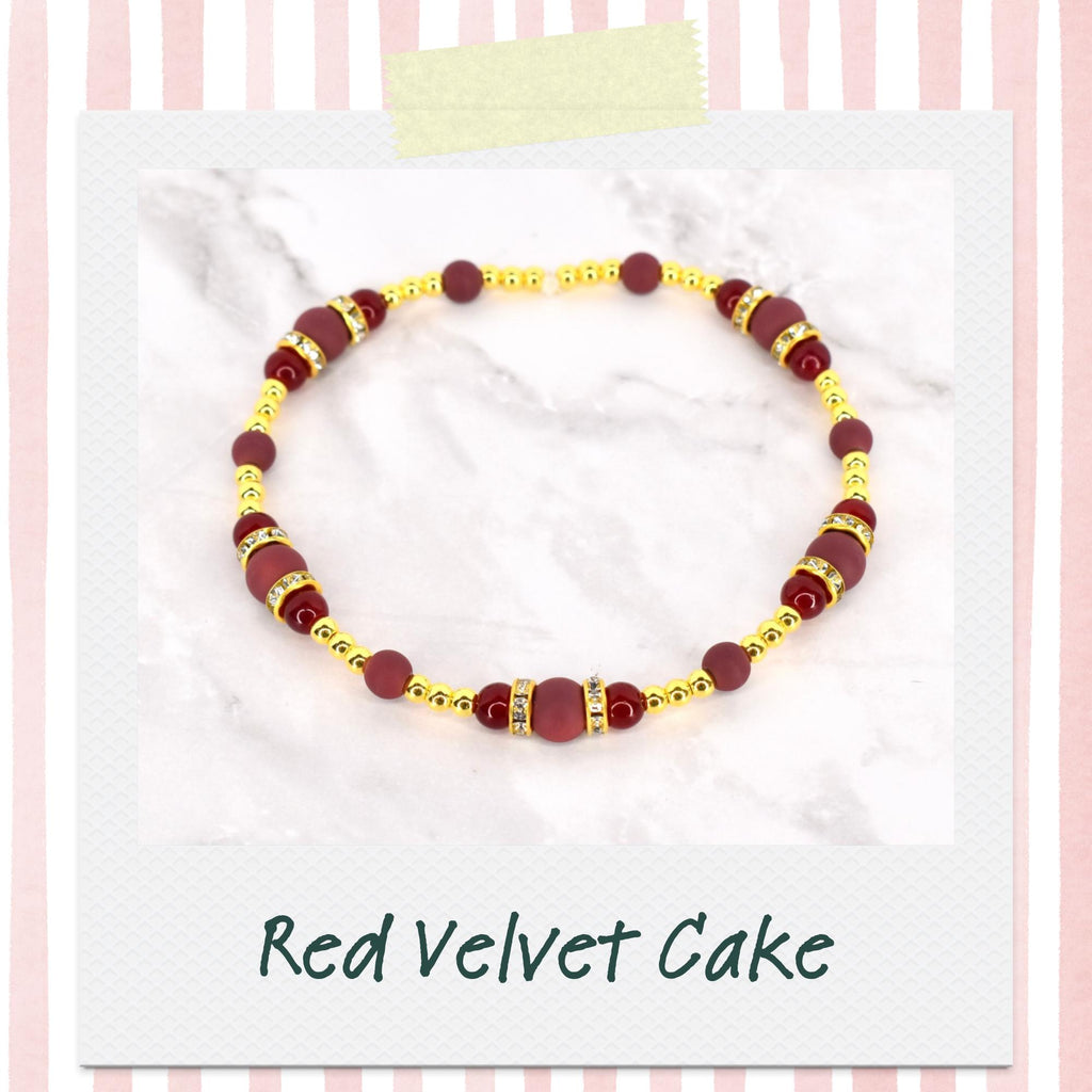 A beaded bracelet with a red velvet cake theme. The bracelet features burgundy and gold beads, with the text "Red Velvet Cake" at the bottom. The bracelet is on a white background.