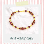 A beaded bracelet with a red velvet cake theme. The bracelet features burgundy and gold beads, with the text "Red Velvet Cake" at the bottom. The bracelet is on a white background.
