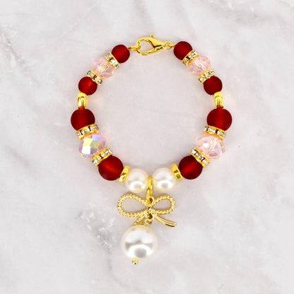 A beaded Stanley handle charm bracelet featuring deep red and light pink beads, accented with gold-colored spacers and a gold bow charm with a dangling white pearl. The bracelet is secured with a gold lobster clasp.