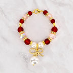 A beaded Stanley handle charm bracelet featuring deep red and light pink beads, accented with gold-colored spacers and a gold bow charm with a dangling white pearl. The bracelet is secured with a gold lobster clasp.