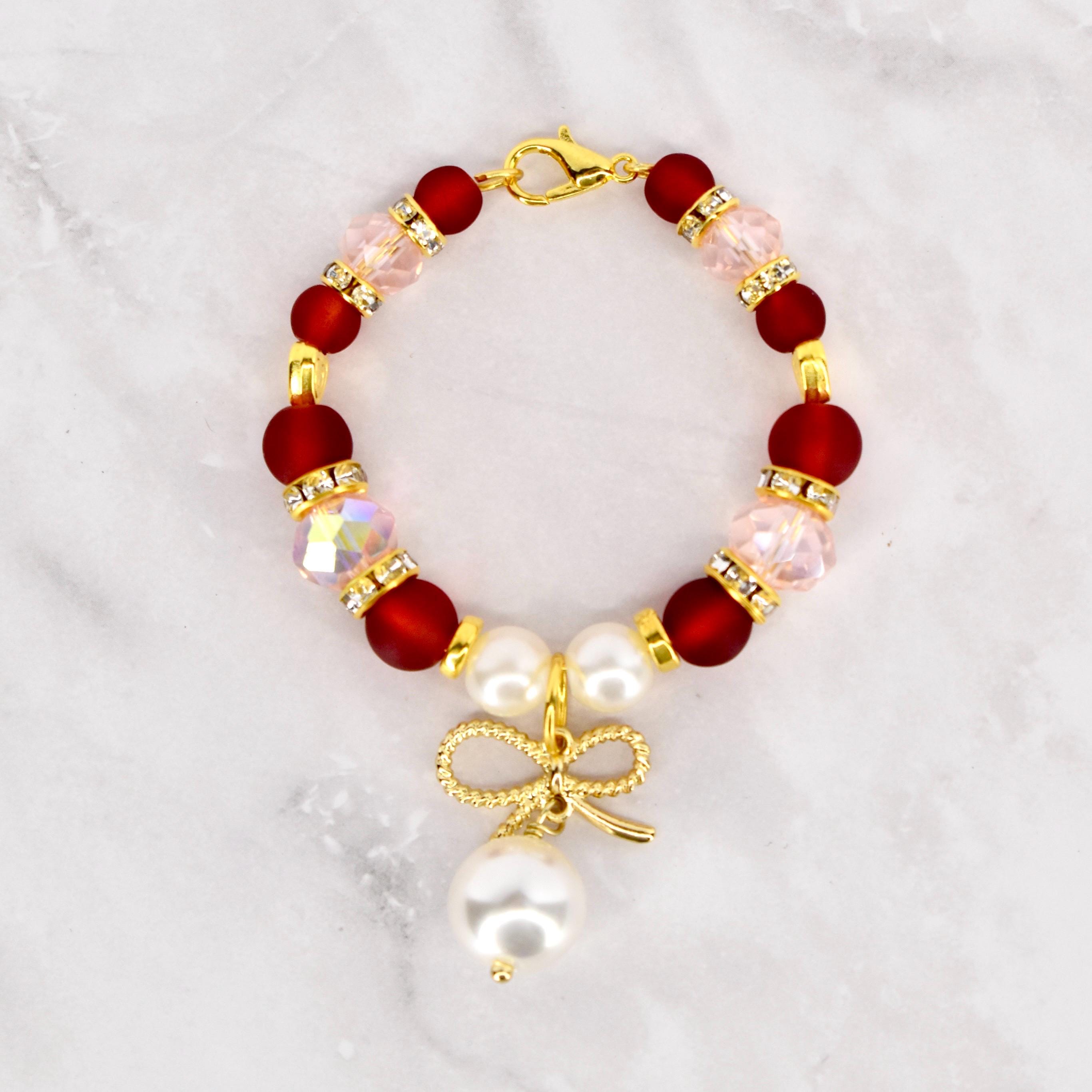 A beaded Stanley handle charm bracelet featuring deep red and light pink beads, accented with gold-colored spacers and a gold bow charm with a dangling white pearl. The bracelet is secured with a gold lobster clasp.