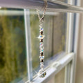 A decorative window sun catcher featuring a silver chain with a lobster clasp, clear and iridescent beads, and a faceted crystal ball at the bottom. The beads are interspersed with silver-colored spacers.