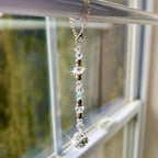 A decorative window sun catcher featuring a silver chain with a lobster clasp, clear and iridescent beads, and a faceted crystal ball at the bottom. The beads are interspersed with silver-colored spacers.