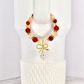 A beaded tumbler handle bracelet with red, pink, and gold accents. The bracelet features a gold bow charm with a dangling pearl. The bracelet is displayed on a white Stanley.