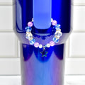 A beaded bracelet with blue, clear, and pink beads, and a star charm. The bracelet is displayed on a blue tumbler. The beads are faceted and round, with silver-colored spacers. The star charm is outlined in silver.