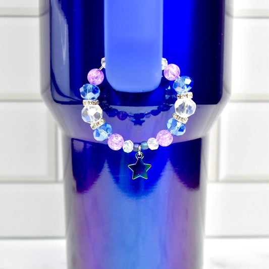 A beaded bracelet with blue, clear, and pink beads, and a star charm. The bracelet is displayed on a blue tumbler. The beads are faceted and round, with silver-colored spacers. The star charm is outlined in silver.