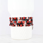 Stack of beaded bracelets in red, black, and silver. The bracelets feature various bead shapes and sizes, including faceted beads and small heart charms. The bracelets are displayed on a white cylindrical object.