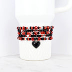 Stack of beaded bracelets in red, black, and silver, wrapped around a white mug. Each bracelet features a mix of beads, with a black heart charm on the bottom bracelet. The bracelets are a mix of faceted and round beads.
