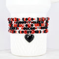 Stack of beaded bracelets in red, black, and clear beads with silver heart accents. One bracelet features a black heart pendant. The bracelets are displayed on a white cylindrical base.