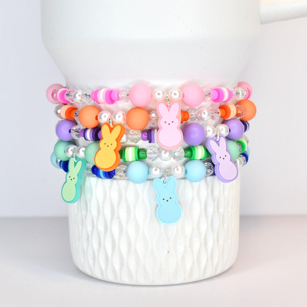 A set of 5 pastel beaded bracelets in pink, orange, purple, green and blue. Each bracelet features a PEEPS bunny charm that matches each of those colors.