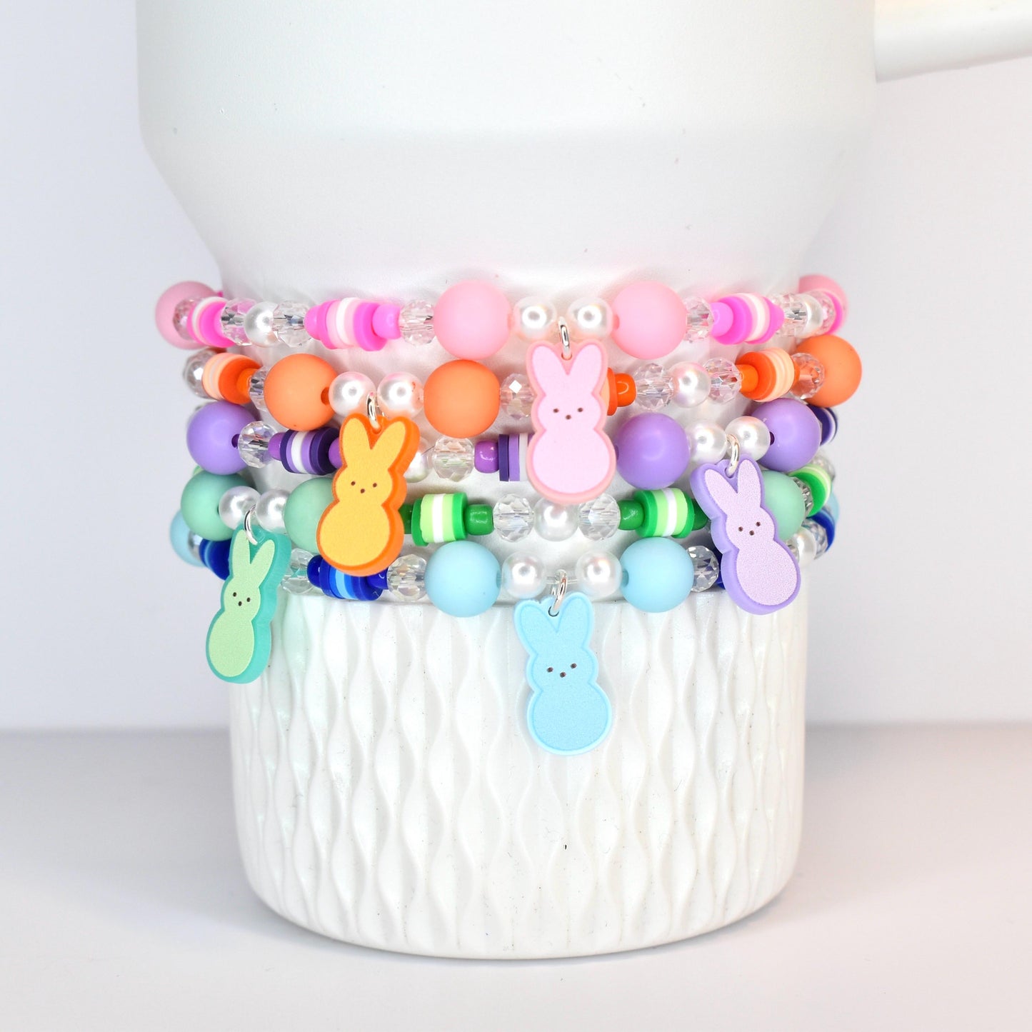 A set of 5 pastel beaded bracelets in pink, orange, purple, green and blue. Each bracelet features a PEEPS bunny charm that matches each of those colors.