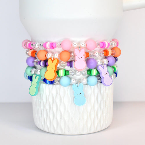 A set of 5 pastel beaded bracelets in pink, orange, purple, green and blue. Each bracelet features a PEEPS bunny charm that matches each of those colors.