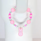 A pink beaded bracelet featuring large round beads, clear crystal beads, and small pink and white rectangular beads. A pink bunny charm hangs from the center. The bracelet is designed for a child.
