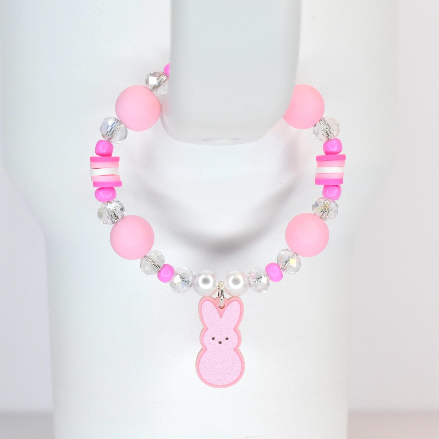 A pink beaded bracelet featuring large round beads, clear crystal beads, and small pink and white rectangular beads. A pink bunny charm hangs from the center. The bracelet is designed for a child.