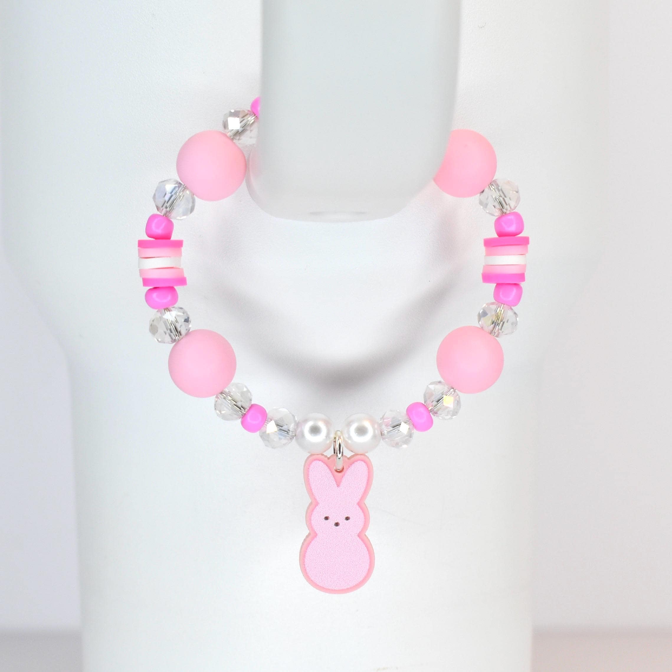 A pink beaded bracelet featuring large round beads, clear crystal beads, and small pink and white rectangular beads. A pink bunny charm hangs from the center. The bracelet is designed for a child.