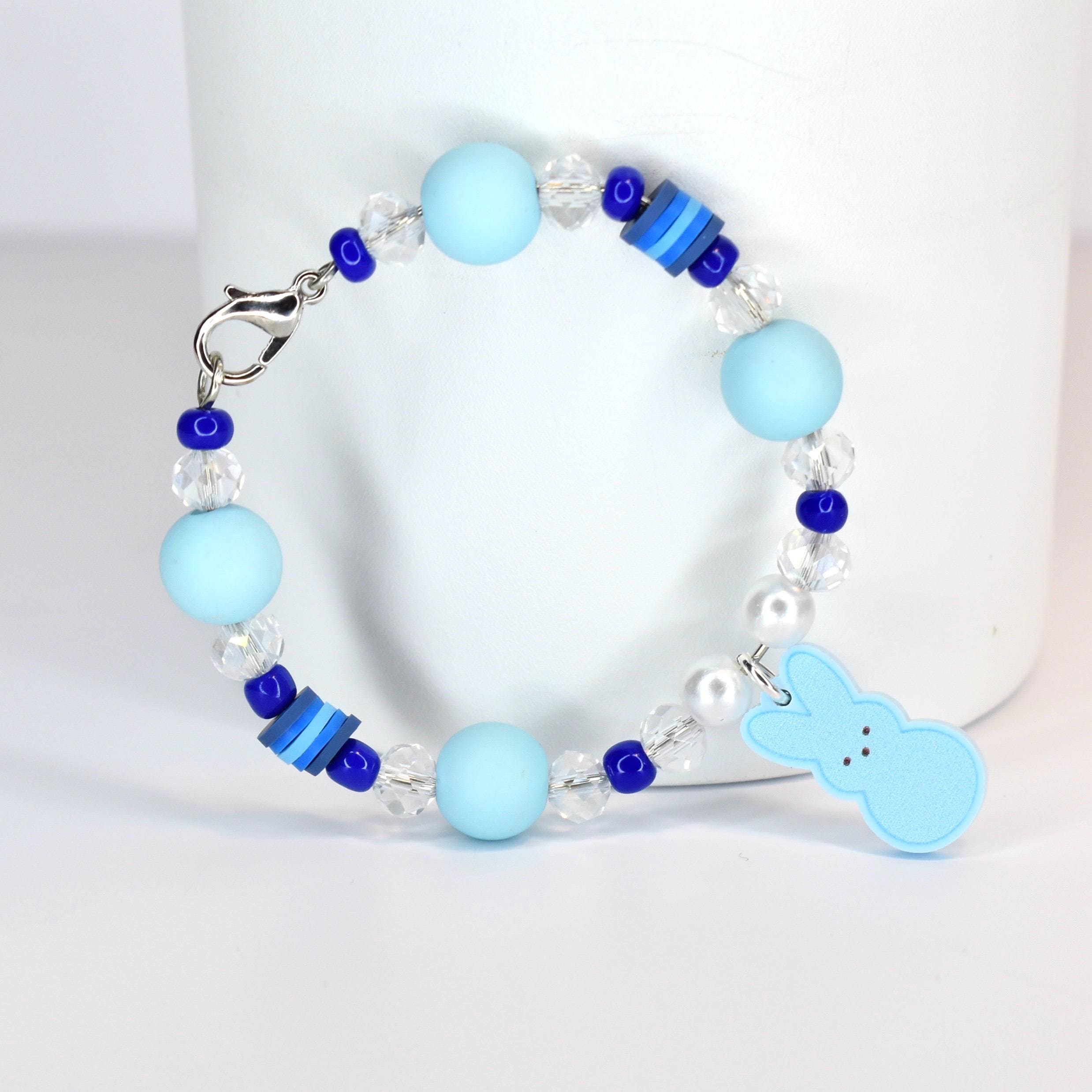 A light blue beaded bracelet with a silver clasp. The bracelet features light blue round beads, clear crystal beads, and dark blue accent beads. A light blue bunny charm hangs from the bracelet.