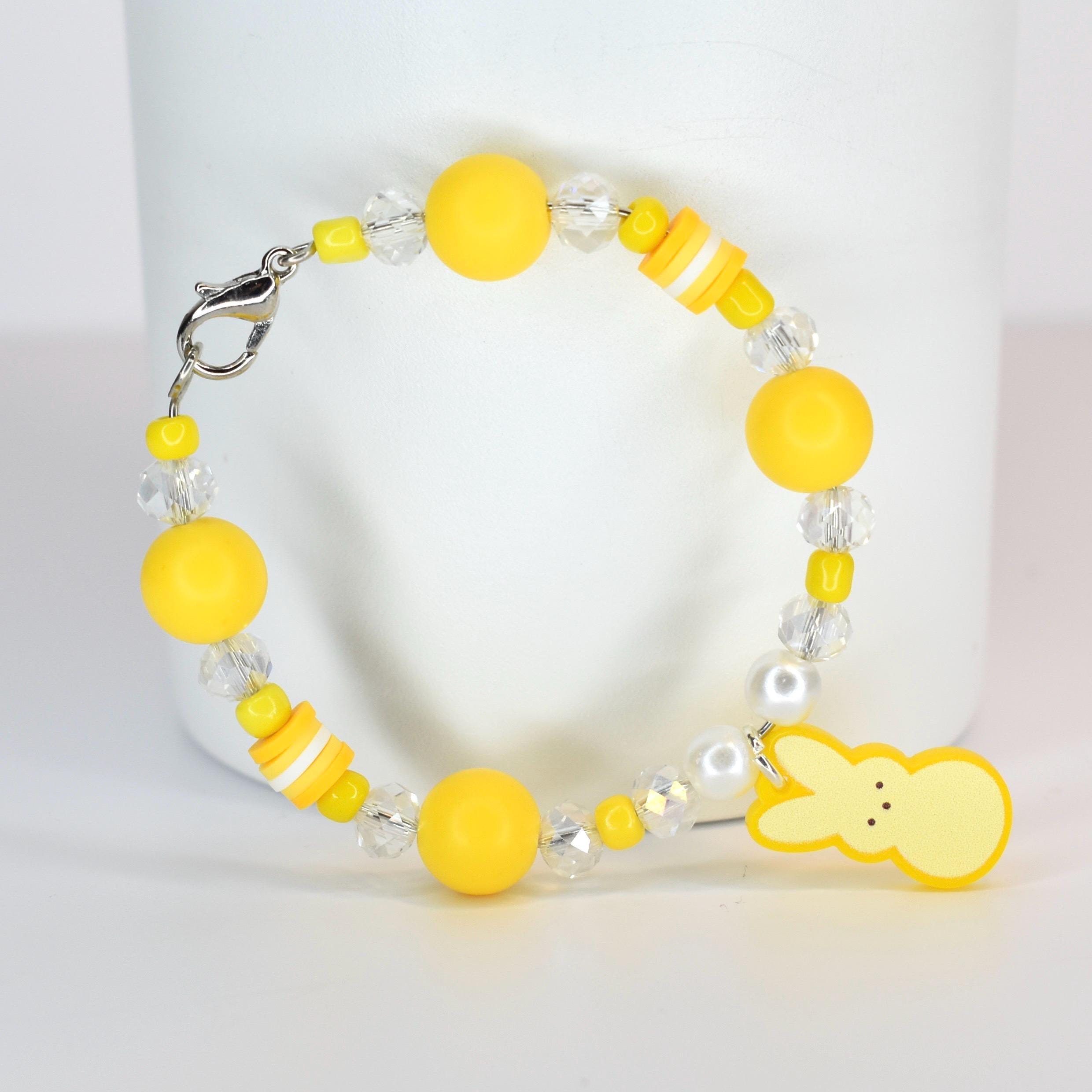 A yellow beaded bracelet with a Peep charm. The bracelet features yellow and clear beads, with a lobster clasp closure. The charm is a yellow Peep shape. The bracelet is a fun, colorful accessory.