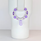 A purple beaded bracelet with a bunny charm. The bracelet features large round purple beads, smaller clear and purple beads, and a dangling purple bunny charm. The bracelet is designed to be worn on the wrist.